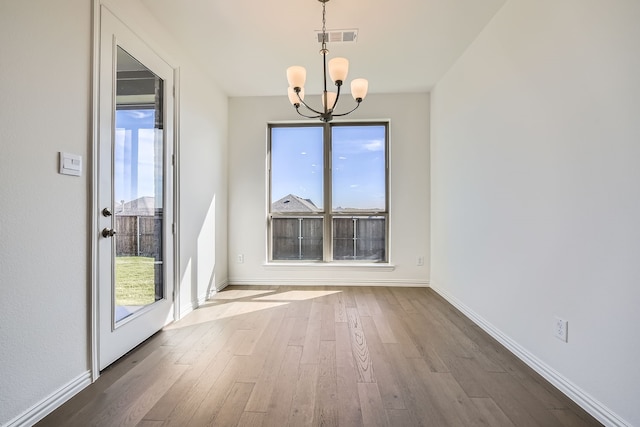 unfurnished dining area featuring a wealth of natural light, an inviting chandelier, and hardwood / wood-style flooring