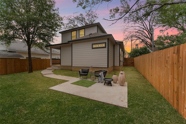 back house at dusk featuring a lawn and a patio