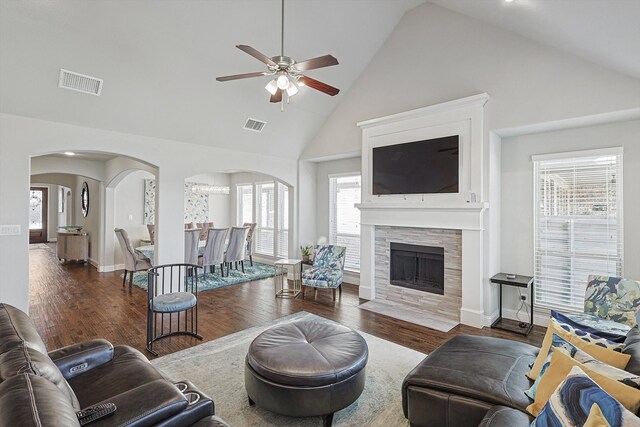 living room with ceiling fan, high vaulted ceiling, dark hardwood / wood-style floors, and a stone fireplace