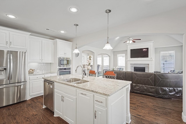 kitchen with an island with sink, sink, decorative light fixtures, appliances with stainless steel finishes, and a fireplace