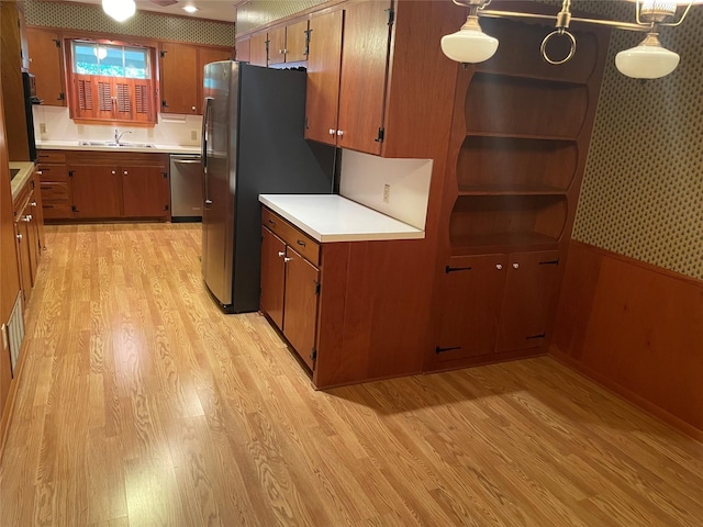 kitchen with stainless steel appliances, sink, decorative light fixtures, light hardwood / wood-style flooring, and wood walls