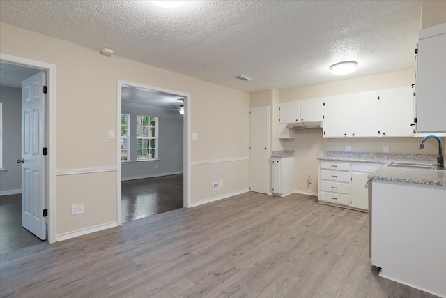 kitchen with sink, white cabinetry, a textured ceiling, and light hardwood / wood-style floors