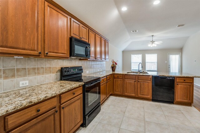 kitchen with sink, light tile patterned floors, light stone counters, black appliances, and kitchen peninsula