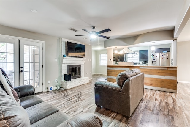 living room with french doors, hardwood / wood-style floors, a brick fireplace, and a wealth of natural light