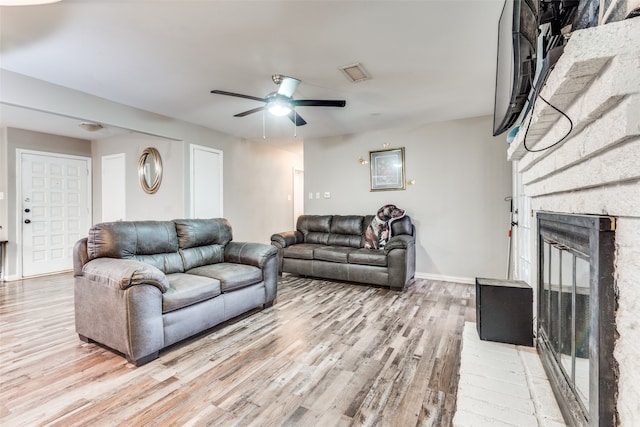 living room with light hardwood / wood-style floors, a brick fireplace, and ceiling fan