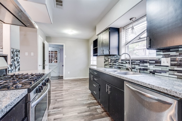 kitchen featuring decorative backsplash, hanging light fixtures, appliances with stainless steel finishes, wood-type flooring, and sink