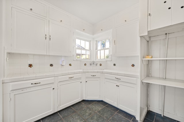 kitchen featuring tile countertops, white cabinetry, sink, and backsplash