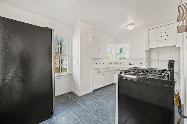 kitchen with white cabinetry, refrigerator, decorative backsplash, and black range oven