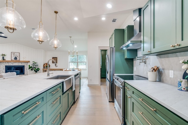 kitchen featuring wall chimney range hood, decorative light fixtures, stainless steel appliances, and green cabinets