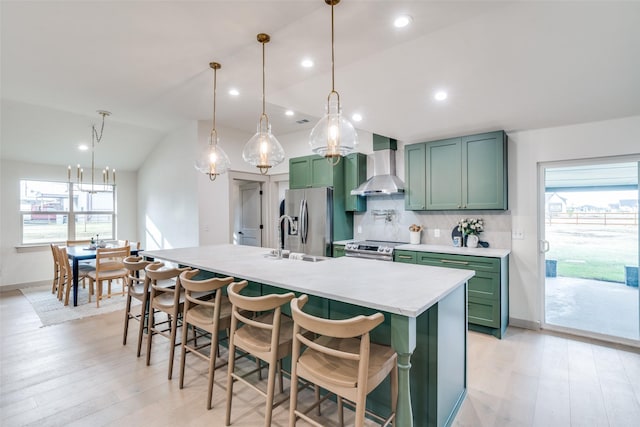 kitchen with pendant lighting, a breakfast bar, appliances with stainless steel finishes, wall chimney exhaust hood, and green cabinetry