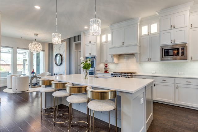 kitchen with white cabinetry, a kitchen island with sink, stainless steel appliances, and hanging light fixtures