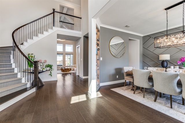 entrance foyer with ornamental molding, a chandelier, dark wood-type flooring, and a high ceiling