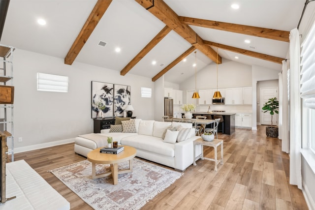 living area with beam ceiling, visible vents, light wood-style flooring, and high vaulted ceiling