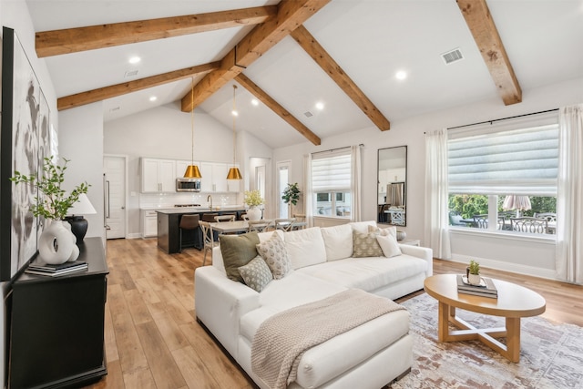 living area with visible vents, a healthy amount of sunlight, high vaulted ceiling, and light wood-type flooring