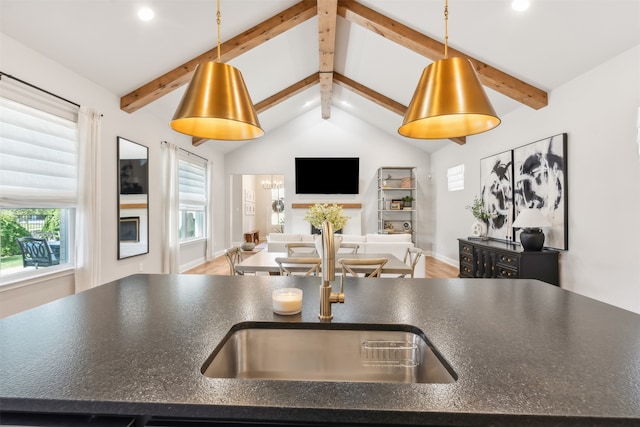 kitchen with pendant lighting, a sink, dark countertops, open floor plan, and vaulted ceiling with beams