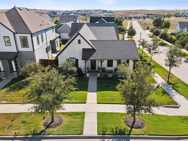 view of front of property featuring a residential view, a shingled roof, a front yard, and stone siding