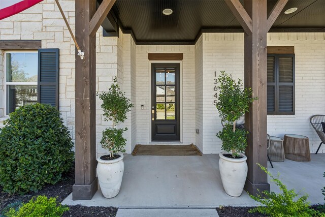 entrance to property with brick siding, covered porch, and a lawn