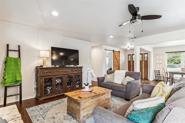 living room with dark wood-type flooring, ceiling fan, and a barn door