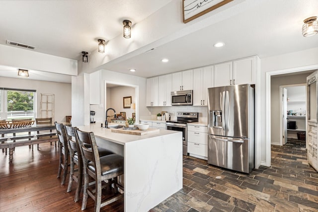 kitchen featuring appliances with stainless steel finishes, a breakfast bar, sink, white cabinets, and a kitchen island with sink