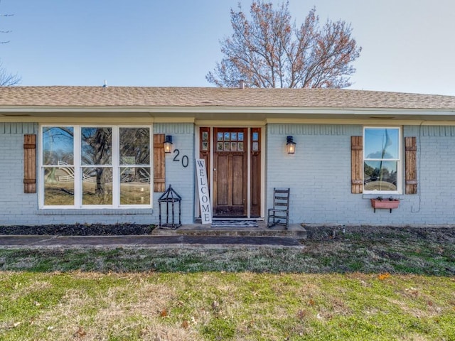 doorway to property with brick siding, a lawn, and a shingled roof