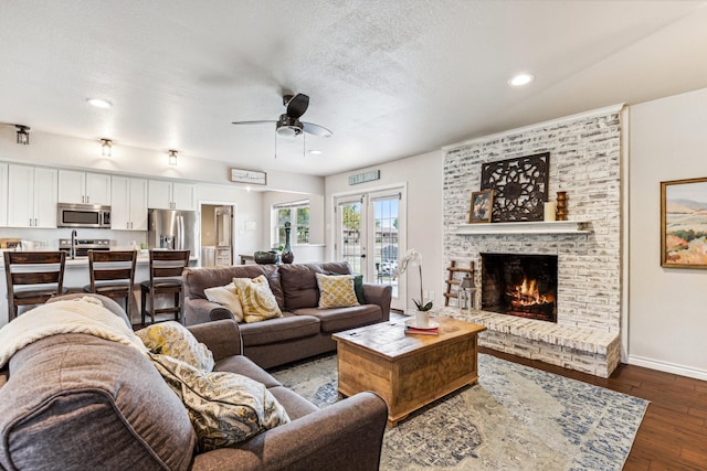 living room with ceiling fan, a brick fireplace, a textured ceiling, and dark hardwood / wood-style flooring