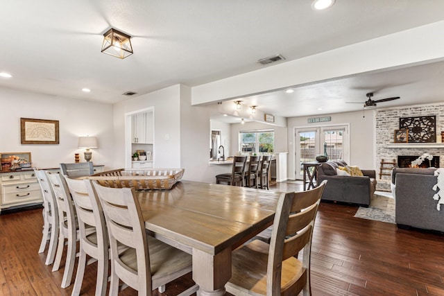 dining space with ceiling fan, a large fireplace, and dark hardwood / wood-style floors