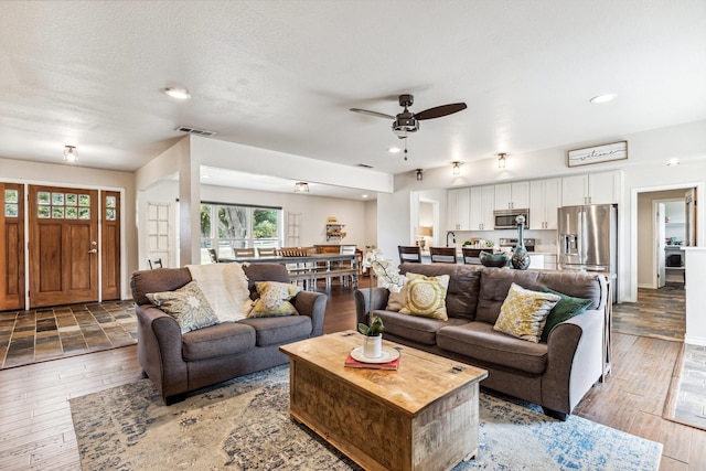 living room with hardwood / wood-style flooring, ceiling fan, and a textured ceiling