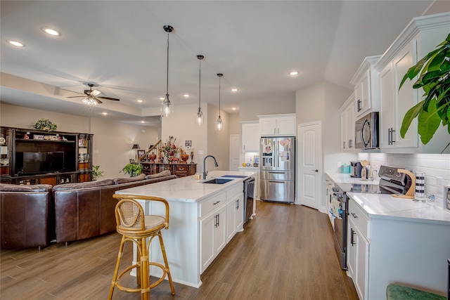 kitchen featuring white cabinets, hanging light fixtures, an island with sink, appliances with stainless steel finishes, and sink