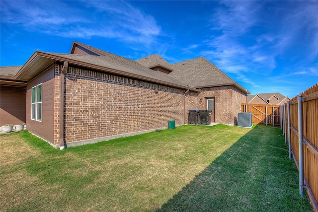 rear view of house featuring central air condition unit and a lawn