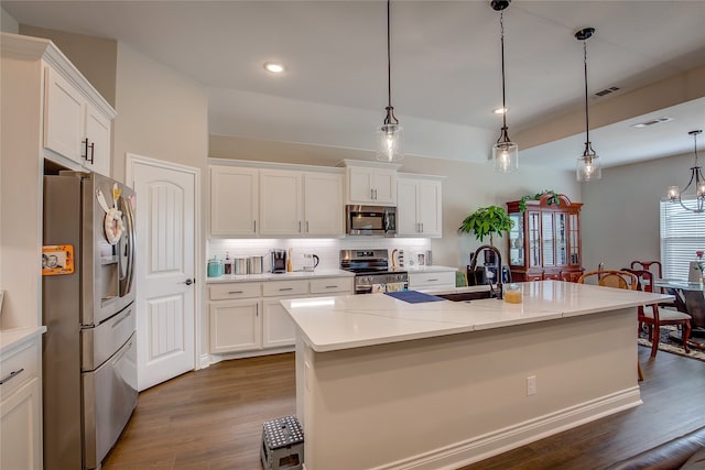 kitchen featuring dark wood-type flooring, appliances with stainless steel finishes, an island with sink, and hanging light fixtures