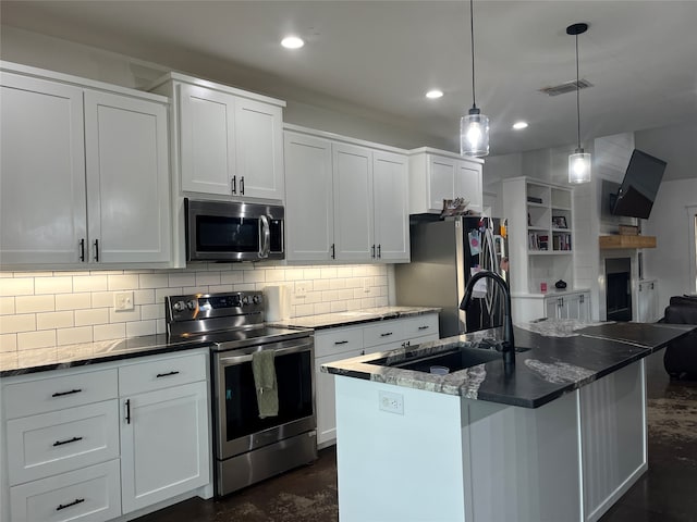 kitchen with appliances with stainless steel finishes, hanging light fixtures, a kitchen island with sink, and white cabinetry