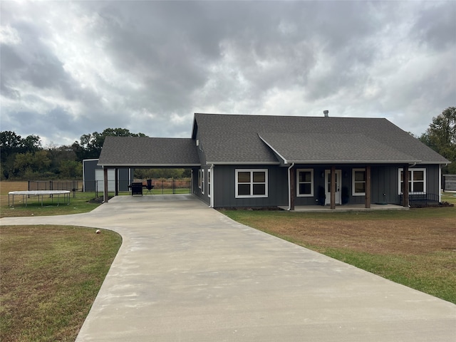 ranch-style home featuring a garage, a carport, a front yard, a trampoline, and a porch