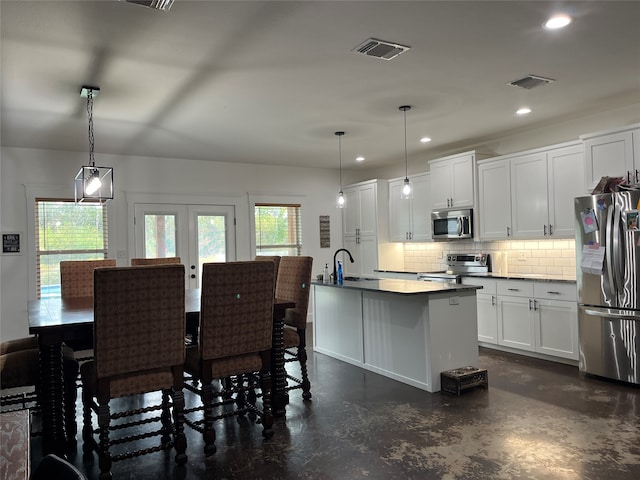 kitchen with white cabinets, stainless steel appliances, a kitchen island with sink, and hanging light fixtures