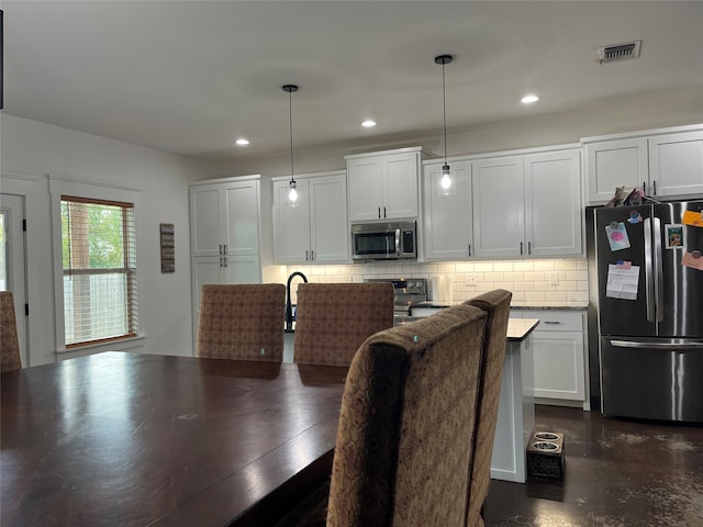 kitchen featuring decorative backsplash, white cabinetry, hanging light fixtures, and stainless steel appliances