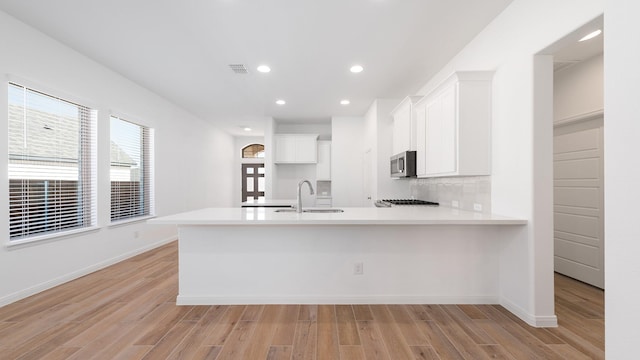 kitchen with sink, white cabinets, decorative backsplash, kitchen peninsula, and light wood-type flooring