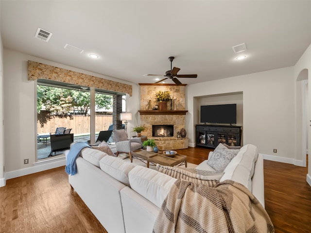 living room with ceiling fan, dark hardwood / wood-style flooring, and a stone fireplace