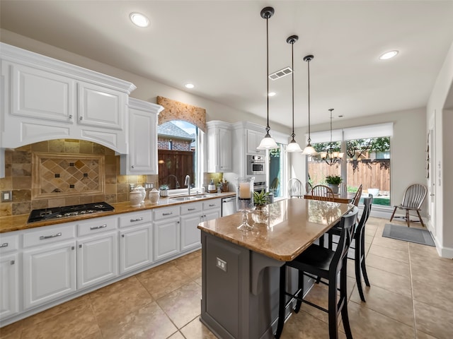 kitchen featuring tasteful backsplash, a kitchen island, white cabinetry, hanging light fixtures, and appliances with stainless steel finishes