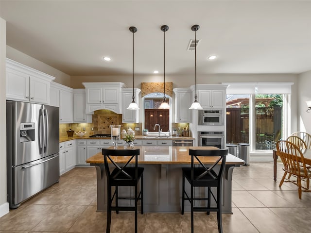 kitchen with white cabinetry, stainless steel appliances, a center island, decorative light fixtures, and sink