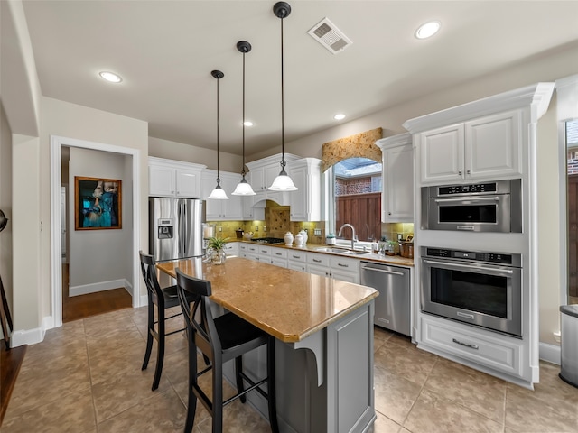 kitchen with appliances with stainless steel finishes, a center island, decorative light fixtures, white cabinets, and sink