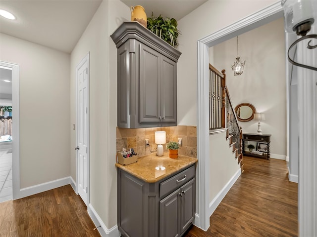 bar featuring tasteful backsplash, light stone countertops, gray cabinetry, and dark hardwood / wood-style floors