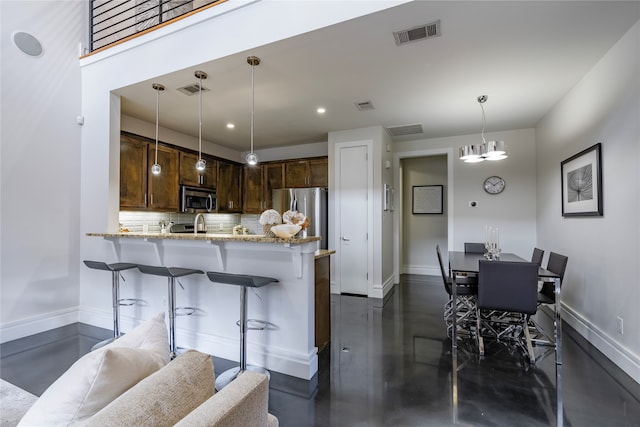 kitchen featuring kitchen peninsula, hanging light fixtures, light stone counters, backsplash, and stainless steel appliances