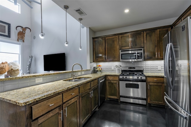 kitchen with kitchen peninsula, light stone counters, appliances with stainless steel finishes, sink, and decorative light fixtures