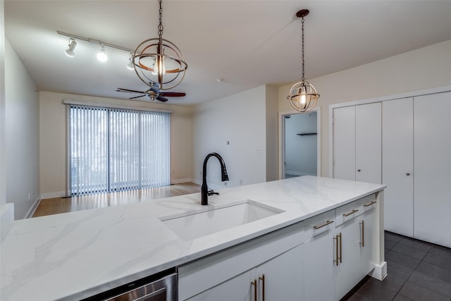 kitchen with light stone counters, sink, white cabinets, and pendant lighting