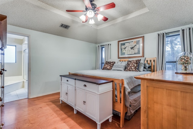 bedroom featuring ensuite bathroom, a raised ceiling, a textured ceiling, ceiling fan, and light hardwood / wood-style flooring