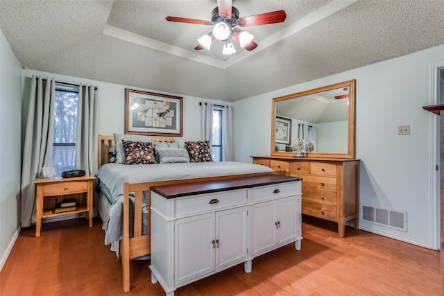 bedroom with ceiling fan, a raised ceiling, a textured ceiling, and light hardwood / wood-style floors