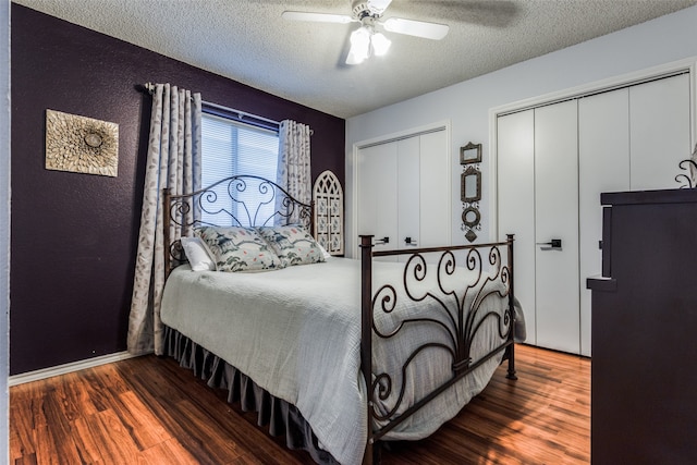 bedroom with dark wood-type flooring, ceiling fan, a textured ceiling, and two closets