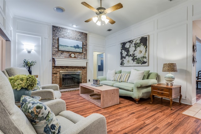 living room featuring a brick fireplace, ornamental molding, wood-type flooring, and ceiling fan