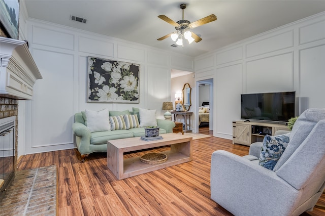 living room featuring a brick fireplace, hardwood / wood-style floors, and ceiling fan