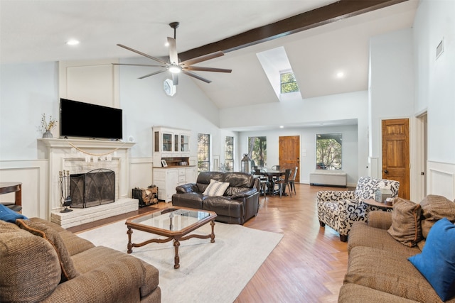 living room featuring light hardwood / wood-style floors, beamed ceiling, ceiling fan, high vaulted ceiling, and a brick fireplace