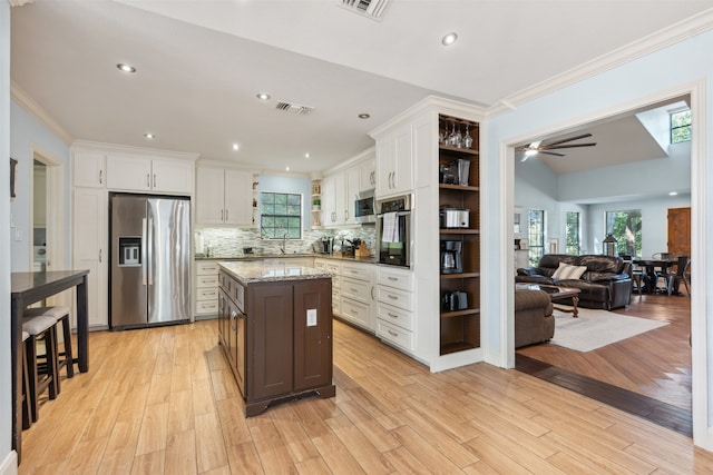 kitchen with white cabinets, light hardwood / wood-style flooring, a kitchen island, light stone countertops, and appliances with stainless steel finishes